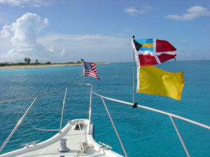 a boat facing the islands in turquoise waters with flag posted on the front