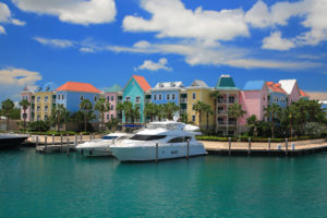private charter flight to the bahamas nassau island with colorful buildings of hotels with a dock in the back equipped with several yachts rested on turquoise, calm waters